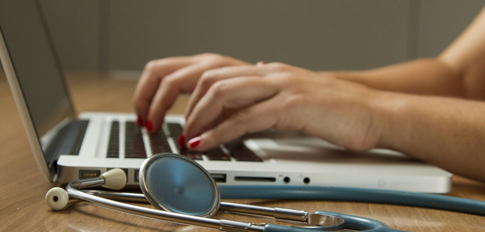 A healthcare practitioner working at a laptop with a stethoscope resting on the desk