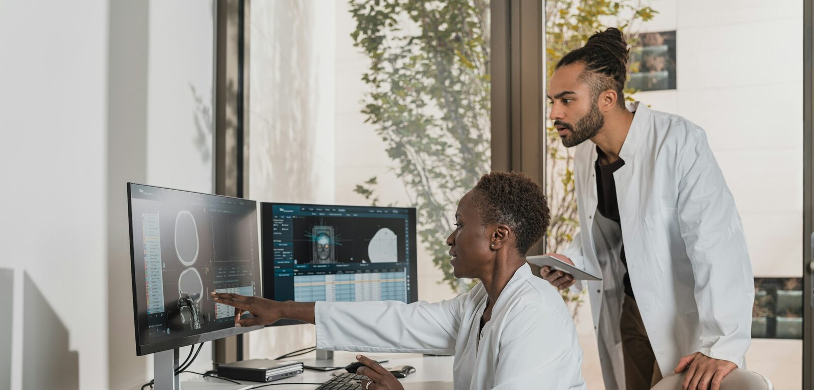 Two doctors reviewing medical scans on computer monitors in a clinic